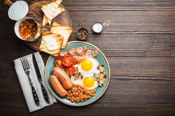 bacon, beans, mushrooms, tomatoes on a plate, bread toasts with butter. Traditional British meal, top view, rustic wooden background, space for text