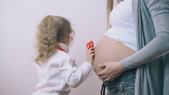 Girl Touches Pregnant Mommy Belly with Toy Stethoscope