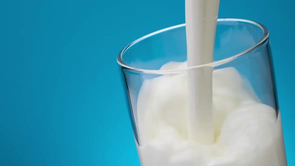 Pouring Milk in Glass Against Blue Background Slow Motion