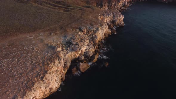 Drone top down aerial view of waves splash against rocky seashore, background. Flight over high clif