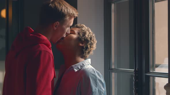 Portrait of Multiethnic Young Couple Standing Near Window and Passionately Kissing