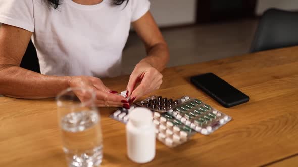 Aged woman take pills from blister pack at home, Headaches, depression