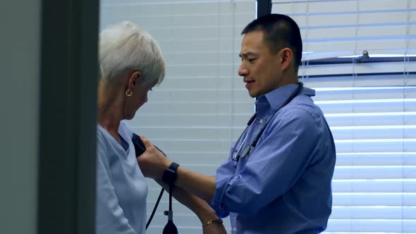 Side view of young Asian male doctor checking blood pressure of senior patient in the clinic 4k