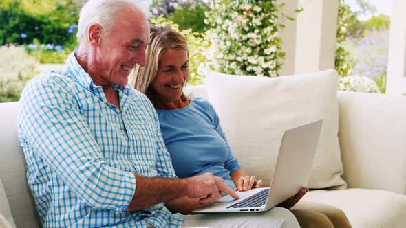 Senior couple interacting with each other while using laptop in living room