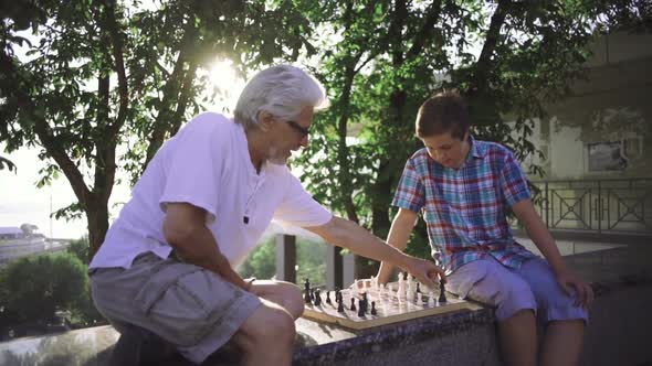 Grandfather and Grandson are Playing Chess in Park