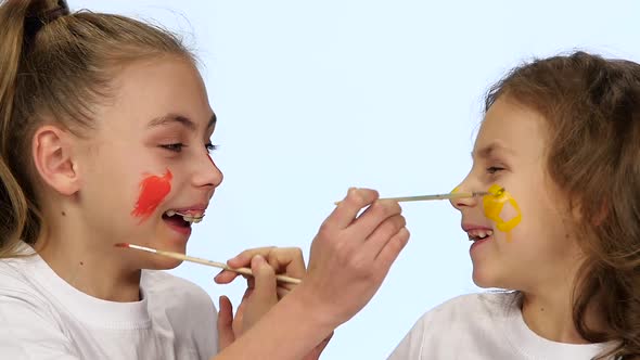 Children Sit at the Table and Paint Themselves on Their Faces with Paint Brushes. White Background