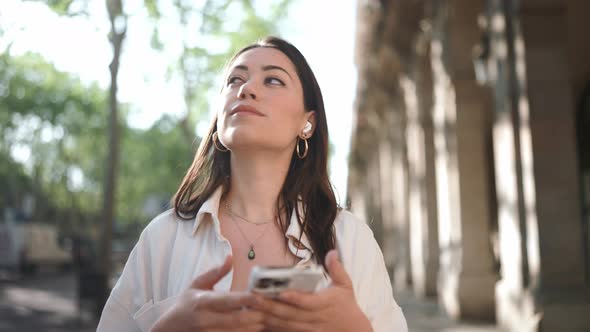 Meditative brunette woman in headphones looking around and texting on phone