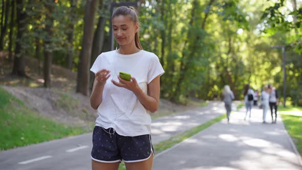 Woman Putting on Earphones To Listen Music Before Jogging Summer Park