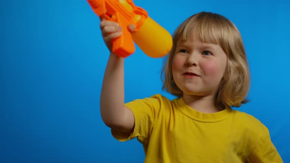 Little Blond Girl in Yellow Tshirt with Orange Water Gun is Laughing in Studio