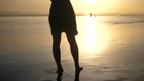 A young woman walks on the beach at sunset.