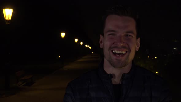 A Young Handsome Man Celebrates in an Urban Area at Night - a Line of Streetlights in the Background