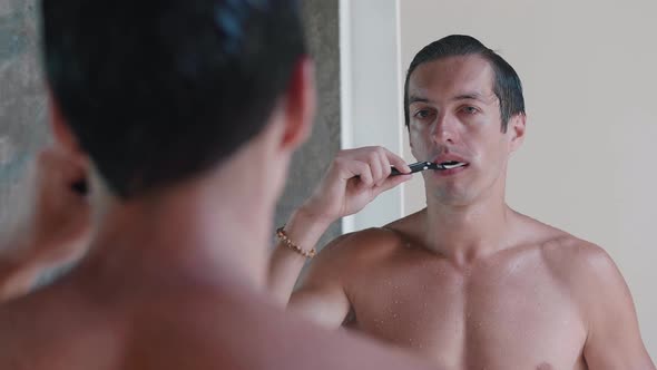 Young Man Brushing His Teeth While Standing in the Bathroom in Front of the Mirror Morning Routine