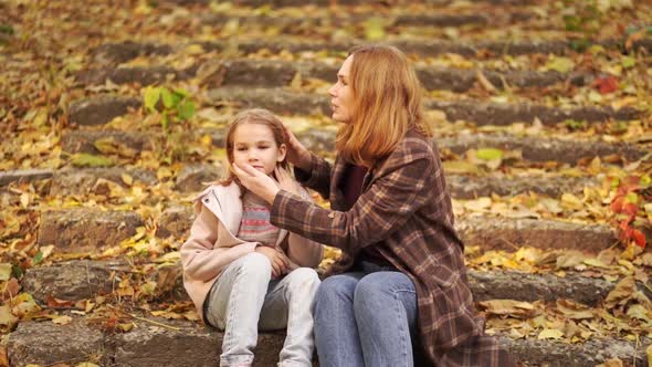 Mother and Daughter Sit and Hug on the Stairs in the Autumn Park