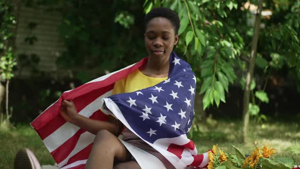 Gorgeous Slim African American Woman Sitting in Garden Wrapping in American Flag Smiling Looking at