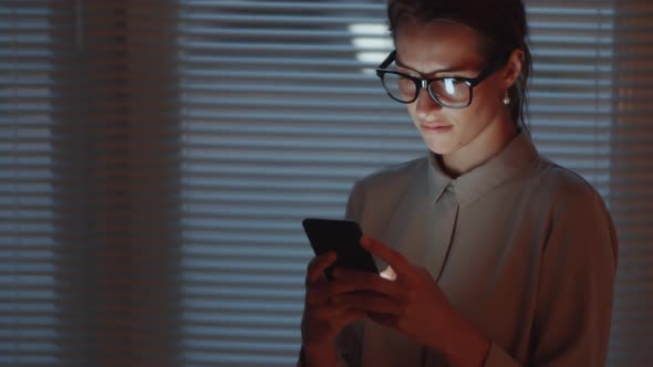 Young Businesswoman Typing on Smartphone in Dark Office