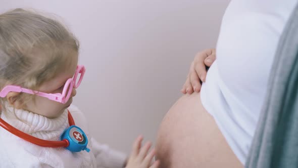 Girl Puts Toy Stethoscope on Pregnant Mother Belly at Home