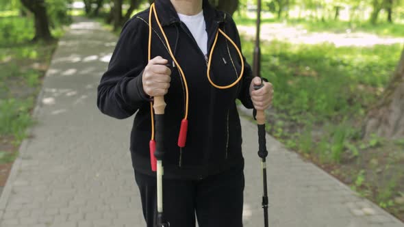 Active Senior Old Woman Training Nordic Walking with Ski Trekking Poles in Park alt