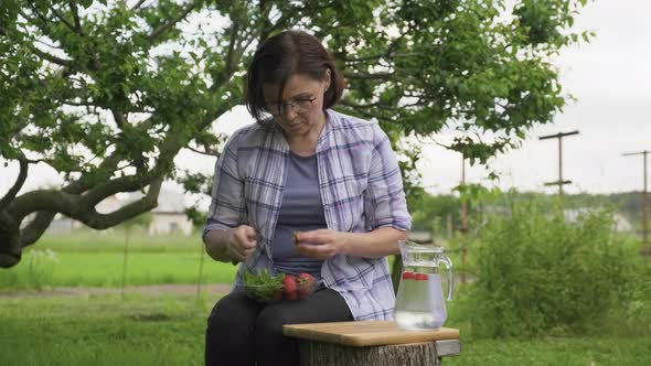 Middle Aged Woman Making Natural Drink with Strawberries and Mint