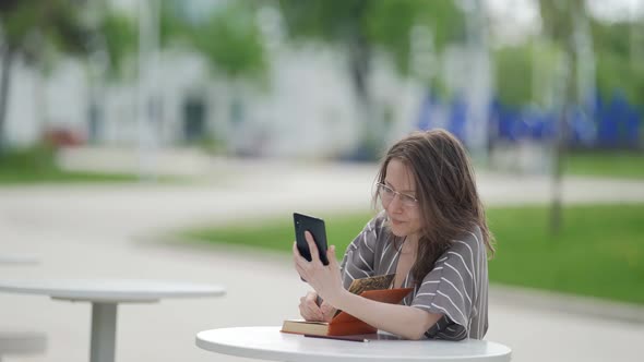 Clever Adult Woman is Studying Online By Smartphone in Park at Summer Day