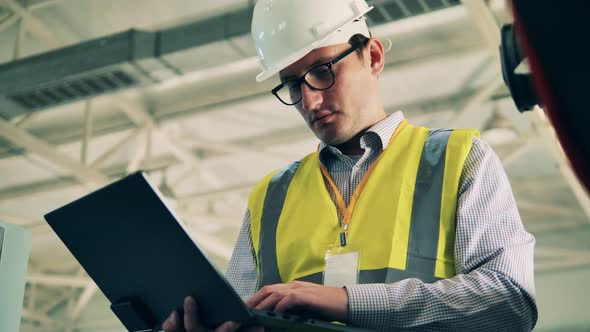 Male Engineer in a Hardhat Is Typing on a Laptop