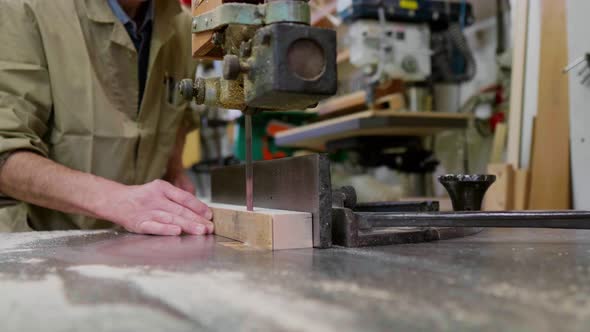 Craftsman sawing wooden bar on band saw in carpentry