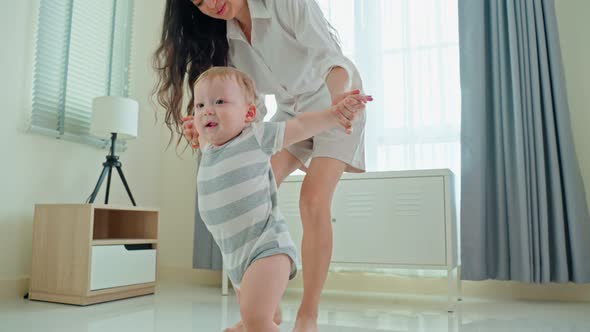 Caucasian baby boy child learn to walk, taking first step on floor with parents support in house.