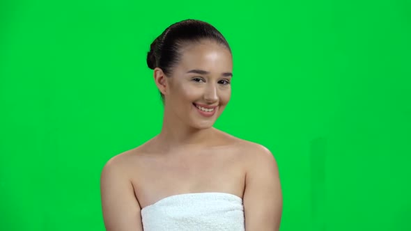 Attractive Woman in White Towel Smiles Coquettishly Looking at the Camera, Green Screen. Slow Motion