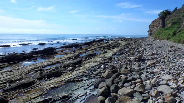 Side view tracking shot of a young man running on a rocky ocean beach shoreline.