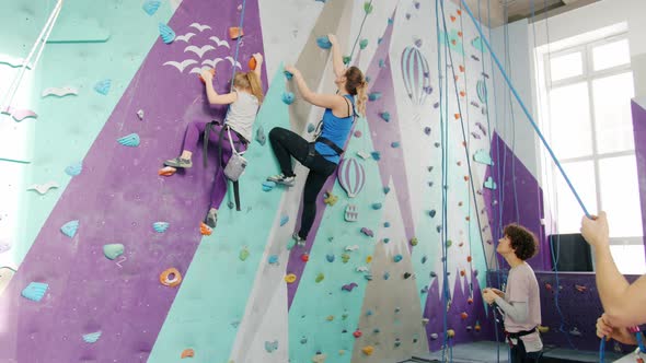 Woman and Kid Enjoying Climbing in Gym While Companions Holding Ropes Standing Below