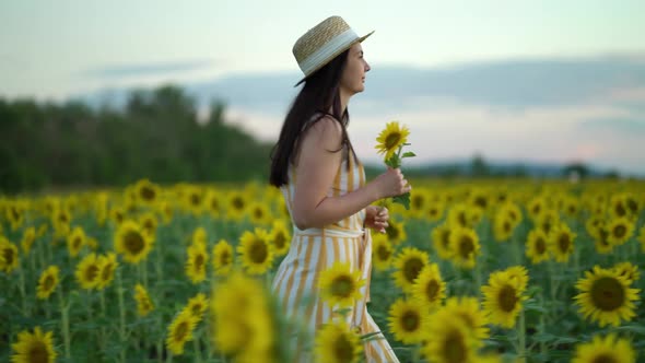 Young Woman in Dress Strolling Through Field with Sunflowers at Sunset