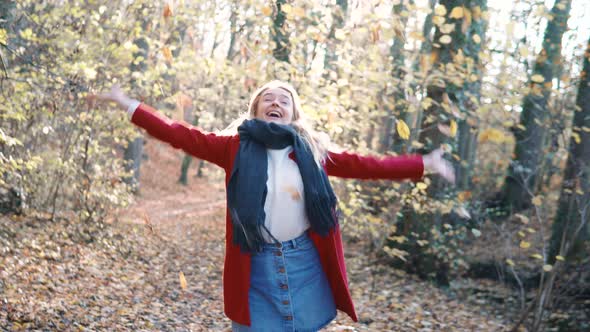Young beautiful woman throwing leaves in the air amidst thee orange brown autumn forest woodland whi