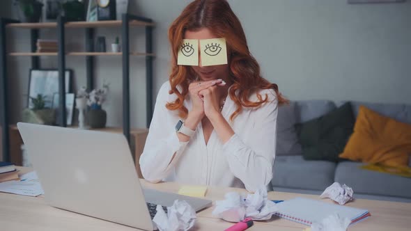 Caucasian Woman Sleeps Sits on Desk with Laptop with Paper Stickers on Eyes