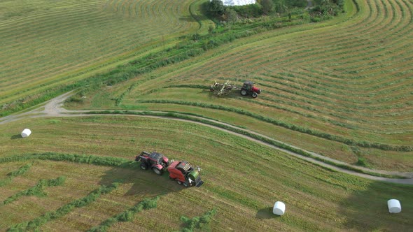 Tractors on farmland collecting fodder and making bales, wraps them in plastic, aerial