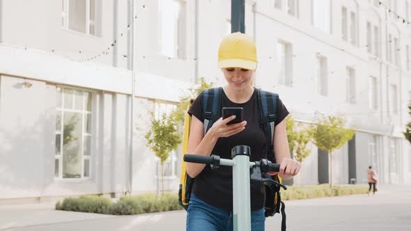 Delivery Woman Using Smartphone While Standing in the City with Electric Push