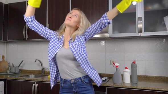 woman in yellow rubber cleaning gloves sings and dances in the kitchen
