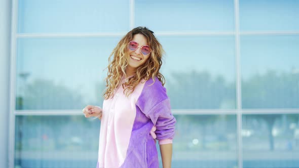 Funny cheerful happy young woman dancing outdoors on blue wall.