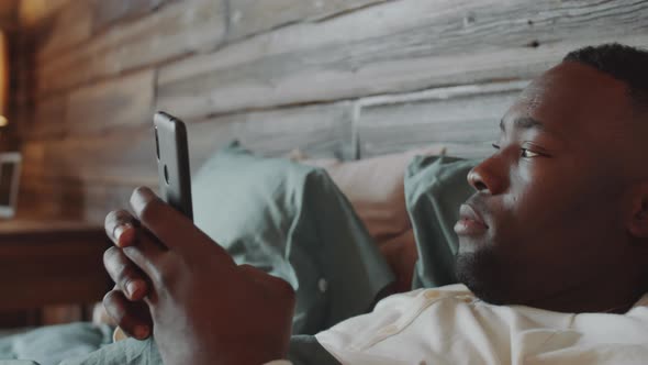 Young Black Man Using Smartphone in Bed