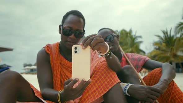 Happy Maasai Tribe Men Sitting on the Sand in the Desert and Looking at the Smartphone