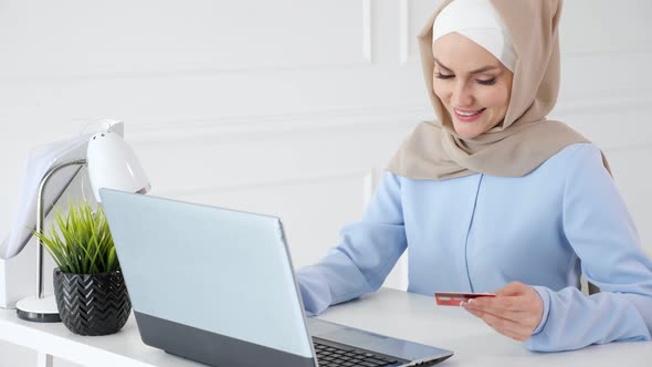Muslim Woman in Hijab is Buying Online with a Credit Card and Laptop