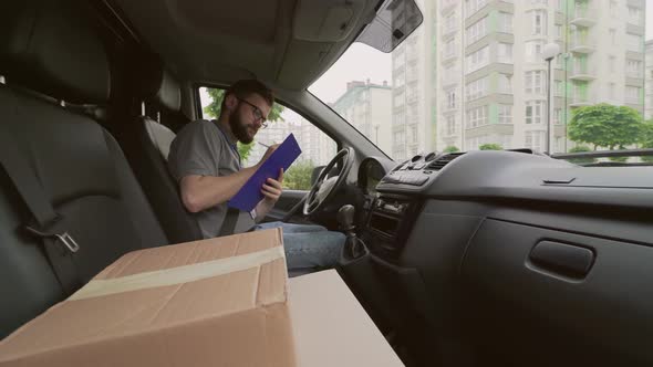 Delivery Man Sitting in Car and Taking Notes in Clipboard