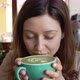 Young Woman in Cafe Takes Sip of Matcha Latte From Cup - VideoHive Item for Sale