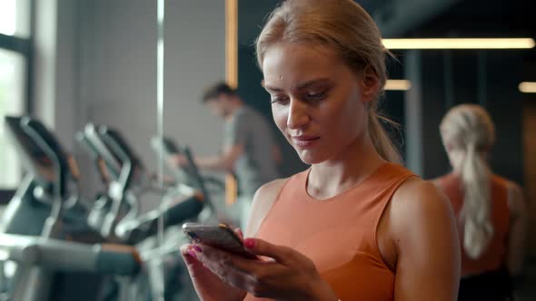 Fit Girl Texting Message at Gym. Sport Woman Using Mobile Phone in Sport Club