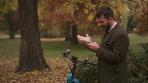 Handsome young man with electric bicycle using mobile phone in the autumn park
