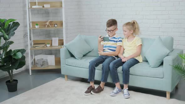 Excited Twins Kids Using Smartphone Sitting Together on Sofa