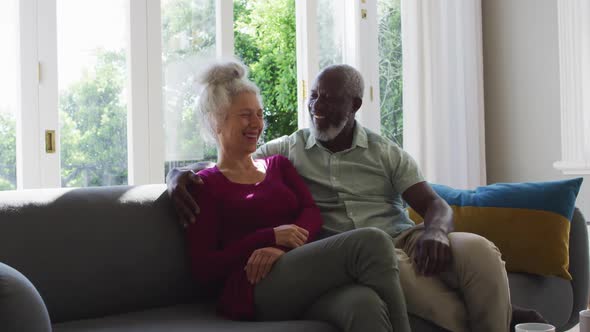 Portrait of mixed race senior couple smiling while sitting on the couch at home