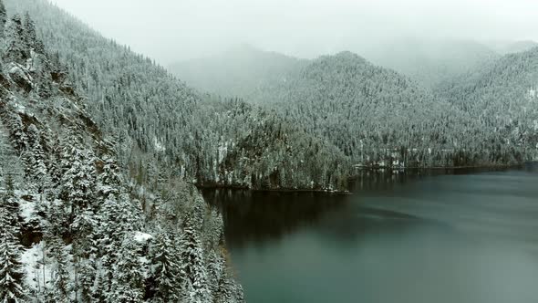 Fantastic aerial view of mountain lake in winter, surrounded by hills, forests.