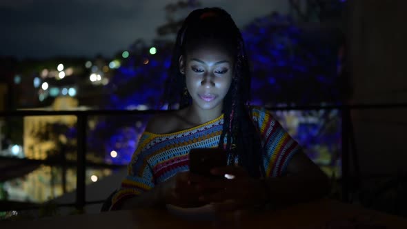 Black woman browsing smartphone in city at night