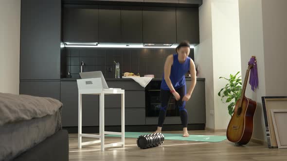 Girl in workout sportswear doing online fitness exercises in kitchen at home during quarantine