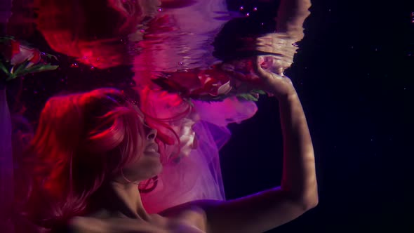 a Woman with Long Red Hair and a Corset Floats in the Dark Under the Water, Touches the Surface with