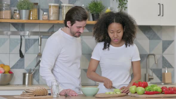 Mixed Race Couple Cutting Vegetables While Standing in Kitchen